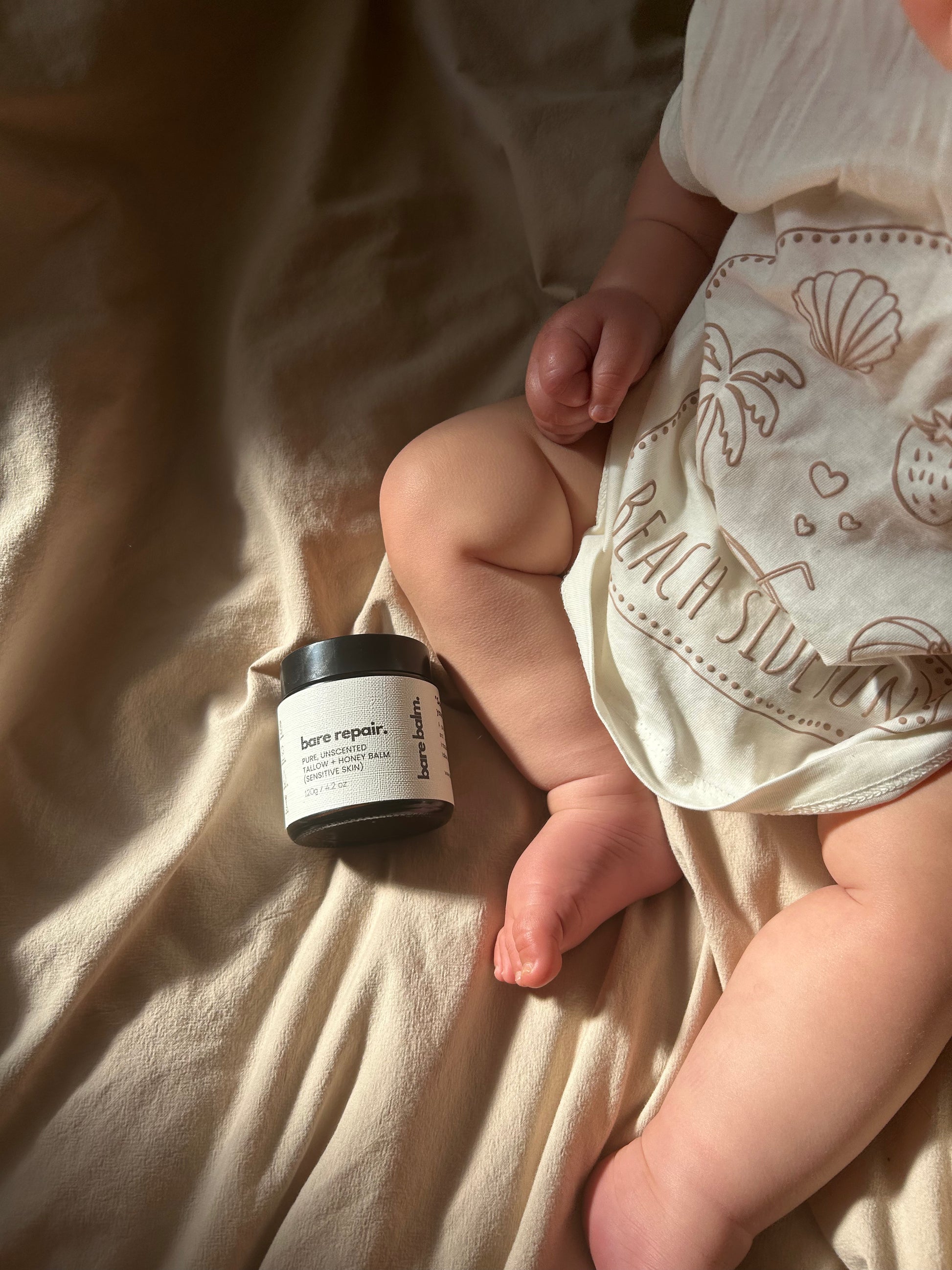 Baby's leg with a jar of cream on a soft fabric background - tallow skincare safe for babies