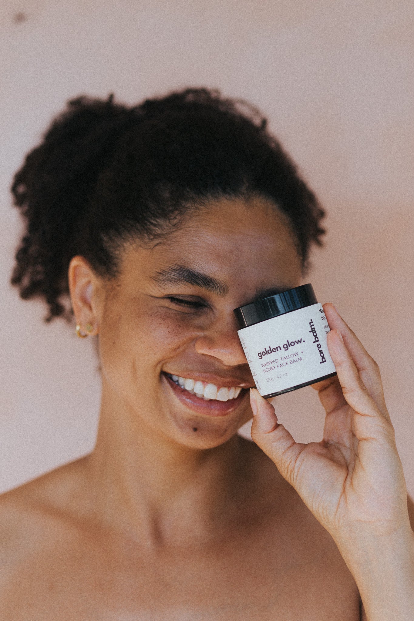 Woman holding a jar of Golden glow body butter against her face.