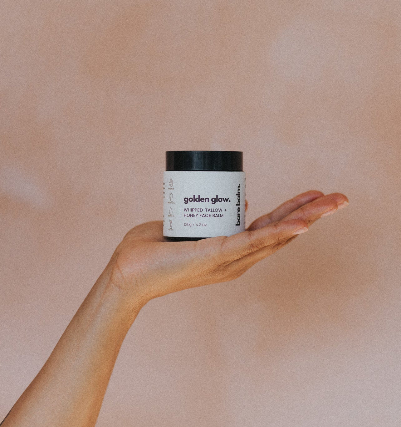 Hand holding a jar of 'golden glow' face balm against a beige background
